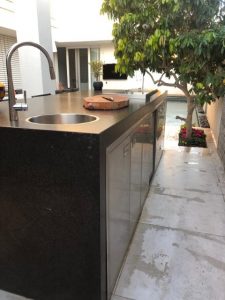 מטבח חוץ משולב בר ישיבה בחיפוי שיש גרניט. מאובזר גריל גז 9 מבערים מבית שאולי, כיור מקרר וארונות אחסון
